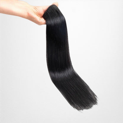 RitzWigs straight natural black human hair clip-in extension held in a hand against a black background